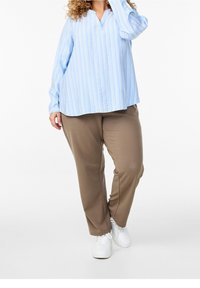 Vaaleansininen raidallinen pitkähihainen paita, jossa on V-pääntie ja rento malli, yhdistettynä ruskeisiin housuihin ja valkoisiin tennareihin. Silkkinen kangas.