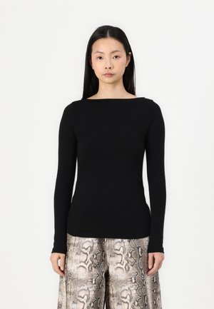 Zwarte top met lange mouwen en een bootneck, gecombineerd met wijde broek met een slangenleerpatroon in beige en grijze tinten.