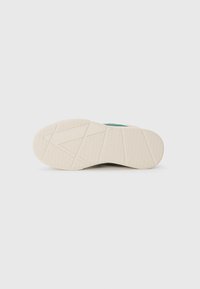 Suola di una sneaker, con una parte inferiore in gomma bianca testurizzata caratterizzata da un motivo geometrico e un accento turchese vicino al tallone.