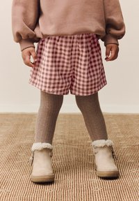 Pantaloni corti a scacchi rosa e marroni abbinati a collant a coste taupe e stivali beige con rifinitura in pelliccia. I pantaloni corti hanno una vita elastica.