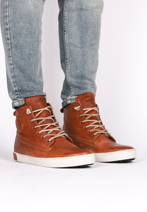 Zapatillas altas de cuero marrón con cordones claros, superficie texturizada y suela de goma blanca. Logo lateral y detalles de costura visibles.