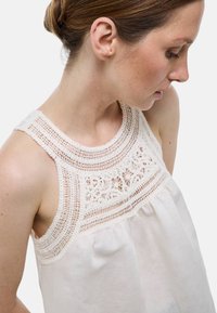 Blouse blanche sans manches avec un empiècement en dentelle texturée et un tissu froncé. Dotée d'un matériau doux et d'une coupe décontractée pour le confort.
