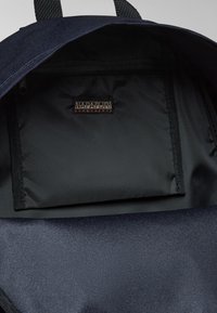 Interno di uno zaino blu navy con una texture liscia e opaca. Presenta una tasca con zip e un'etichetta del marchio "NAPAPIJRI geographic" di colore marrone scuro.