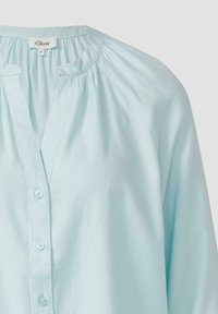 Blusa azzurro chiaro con scollatura rotonda, chiusura a bottoni frontale e dettagli arricciati sulle spalle. Realizzata in tessuto morbido e liscio.