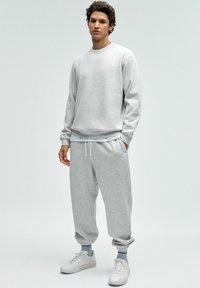 Helehallist sweatshirtist ja sobivatest pükstest, mis on valmistatud pehmest materjalist. Komplektil on elastsed varrukad ja mugav lõige, mida on kombineeritud valgete tossudega.