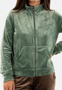 Giacca in fleece verde con colletto alto, zip completa e tasche frontali. Tessuto morbido e design informale, caratterizzato da un colore uniforme e discreto.