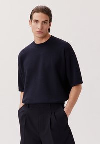 Maglione corto a maniche corte di colore blu navy con un sottile motivo a trama e un collo rotondo, abbinato a pantaloni scuri a vita alta.