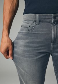 Szare dżinsy o slim fit, z klasycznym pięciopocketowym wzorem, szlufkami na pasek i przeszyciem tylnej kieszeni. Materiał wydaje się miękki i elastyczny.