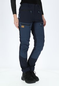 Navy outdoor pants with multiple zippered pockets, contrasting dark panels, elastic waist, and durable fabric; suitable for various activities.