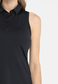 Černé polo tričko bez rukávů z hladké látky, s předním zapínáním na knoflíky a jemným logem na levé straně hrudi.