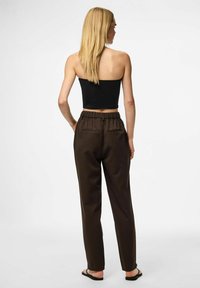 Zwarte cropped tanktop gecombineerd met donkerbruine, high-waisted broeken met een trekkoord in de taille en achterzakken. Model van achteren afgebeeld.