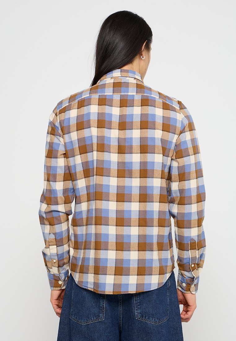 Camicia di flanella a quadri nei colori marrone, crema e azzurro chiaro; maniche lunghe con polsini a bottone; orlo arrotondato; colletto semplice; texture morbida.