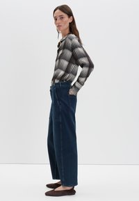 Langsleeve geruit overhemd in zwart-wit, gecombineerd met wijde donkere denim broek en bruine flats, getoond in een zijprofiel.