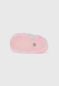 Semelle de chausson rose en peluche avec un motif de points de grip et taille 25 imprimée près du talon, vue de dessous sur fond blanc.