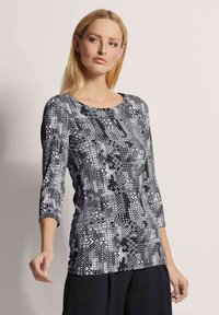 Schwarz-weiß gemustertes Oberteil mit rundem Halsausschnitt und drei Viertelärmeln, das geometrische Designs und eine glatte Textur aufweist.