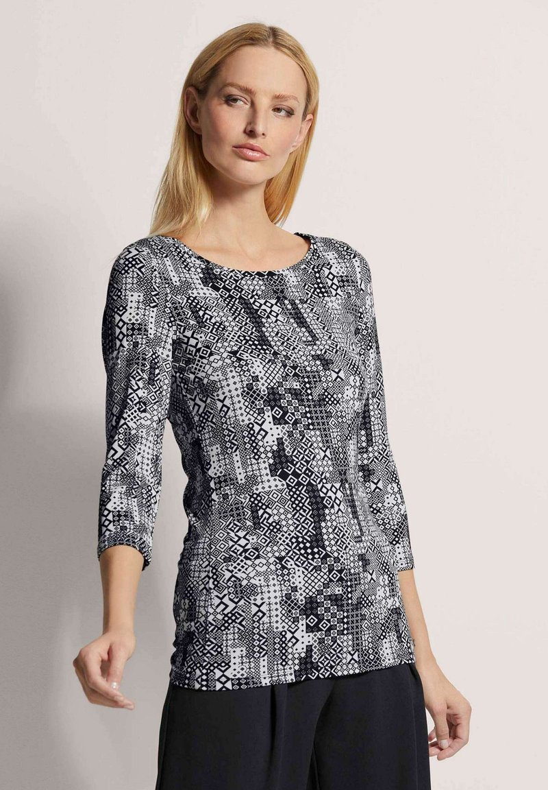 Schwarz-weiß gemustertes Oberteil mit rundem Halsausschnitt und drei Viertelärmeln, das geometrische Designs und eine glatte Textur aufweist.