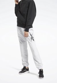 Top largo negro acolchado de manga larga combinado con pantalones blancos de puños elásticos que presentan un acento negro estampado. Unos zapatos deportivos negros completan el conjunto.