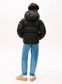 Veste noire matelassée avec capuche, présentant un design matelassé. Assortie à un jean bleu clair et des baskets beiges. Look simple et fonctionnel.