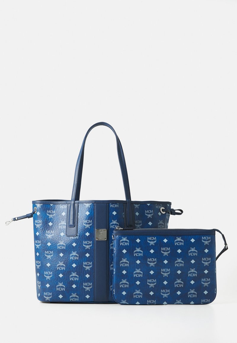 Geantă tote din piele albastră și pouch cu fermoar asortat, cu un model repetat al logo-ului alb, prevăzute cu două mânere, expuse pe un fundal alb.