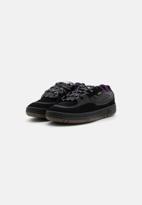 Adidași negri din suede cu un model texturat, având accente mov și o talpă din cauciuc. Sunt incluși șireturi reflectorizante.