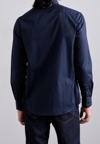 Navyblaue Langarmbluse aus glattem Baumwollstoff, mit einem knopfbaren Kragen, Einzelmanschetten und einem geraden Schnitt am Saum.