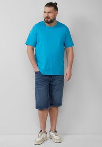 Jasnoniebieska koszulka z krótkim rękawem, zestawiona z ciemnoniebieskimi szortami dżinsowymi, noszona z kremowymi i czarnymi trampkami, na jednolitym tle.