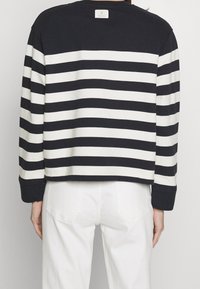 Dlouhý rukáv, tričko s kulatým výstřihem v námořnické modro-bílé pruhy. Materiál je bavlna, na zadním výstřihu se nachází značková etiketa. Casual design.