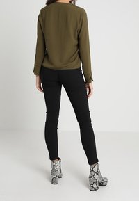 Olivenfarbener Langarm-Top aus strukturiertem Stoff, schwarze Slim-Fit-Hose und Stiefeletten mit einem Schlangenledermuster in Schwarz und Weiß.