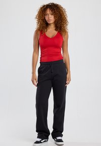 Red sleeveless top with a v-neck, paired with black sweatpants featuring an elastic waistband and drawstring, completed with black sneakers.
