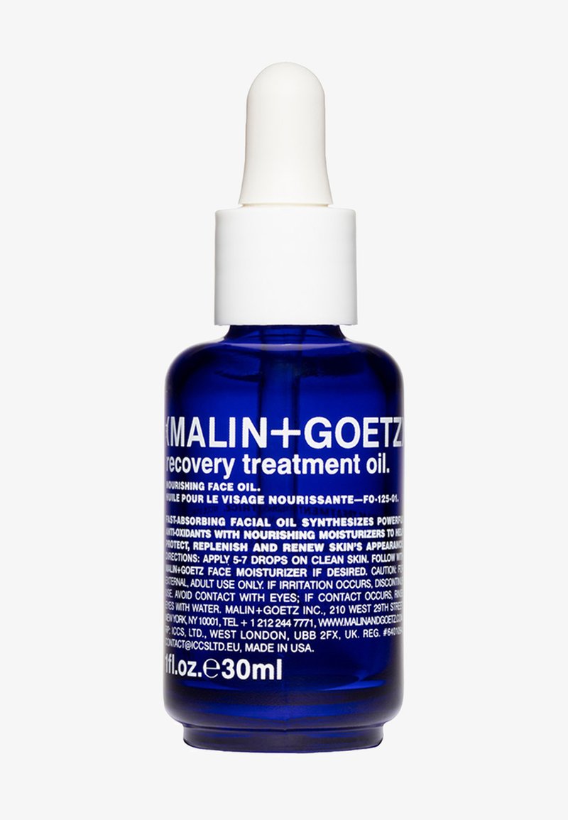 Bottiglia di vetro blu con contagocce e tappo bianco, etichettata "Malin + Goetz Recovery Treatment Oil." Il testo include istruzioni e dettagli sull'uso.