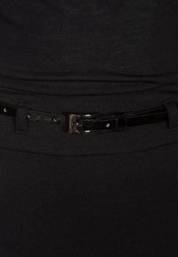 Ceinture en tissu noir avec une ceinture en cuir verni noir brillant. La ceinture possède une boucle métallique rectangulaire et de petits trous circulaires.
