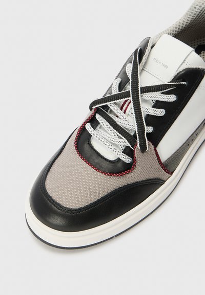 Sneaker con tomaia grigia in mesh, dettagli in pelle nera, lacci bianchi e cuciture rosse; punta arrotondata e suola testurizzata.