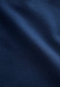 Tissu bleu foncé lisse avec une texture fine en tricot et des plis doux, montrant de subtiles variations de lumière et d'ombre.
