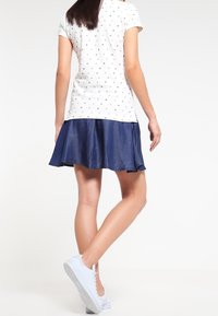 Modrá džínová sukně s rozšířeným střihém, zkombinovaná s bílým tričkem s krátkým rukávem, které má malé černé tečky. Na nohou má světle modré tenisky.