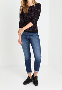 Top a maniche lunghe nera con piccoli pois rosa e bianchi, abbinato a jeans blu con risvolto e sneakers nere. Tessuto morbido e vestibilità casual.