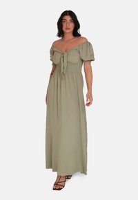 Olivgrön maxiklänning med avtagbara puffärmar, knyt-fram detalj, smockad bodice och flödande kjol. Bärs med svarta sandaler med remmar.