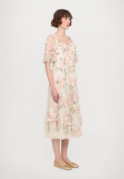 Florale chiffon jurk met korte, gerimpelde mouwen. Kenmerkt zich door gelaagde lagen en zachte roze en groene patronen. Draagt met gouden, gevlochten platte schoenen.