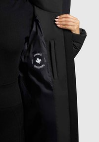 Cappotto esterno nero con fodera nera in satin, dotato di un’etichetta con logo e una tasca laterale interna, texture liscia e design su misura.