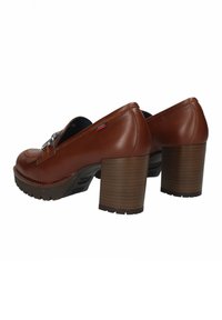 Scarpe con tacco alto in pelle marrone con punta arrotondata, cuciture decorative e tacco in legno texturizzato. Suola in gomma per una migliore aderenza.