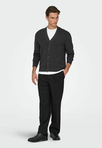 Cardigan grigio scuro con scollo a V, chiusura frontale con bottoni e maniche lunghe abbinato a pantaloni neri e scarpe nere. Design semplice e strutturato.