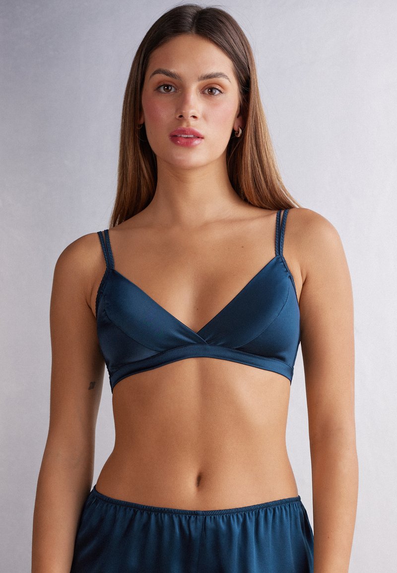 Türkiser Satin-Bralette mit einem Überkreuz-Design, dünnen verstellbaren Trägern und weicher Textur. Das Model trägt dazu passende Unterteile.