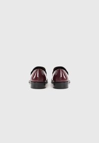 Des chaussures en cuir verni bordeaux avec un bout arrondi et une semelle en caoutchouc noir. Le design présente une finition lisse et des accents de couleur contrastants.