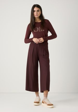 Bordeaux langärmelig top met een logotype van rhinestones, gecombineerd met hoge taille, wijde broek en beige gestructureerde sneakers.