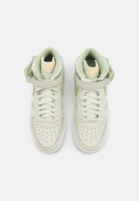 High-top sneakers made of light green leather with perforated toe, white sole, and adjustable strap. Features Nike branding in yellow.