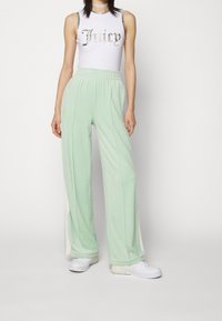 Bílý bezramínkový top s nápisem "Juicy" ve stříbrných písmenech, spárován s mentolově zelenými širokými kalhotami s kontrastní bílou boční částí.