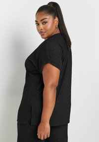 Czarna bluzka z krótkim rękawem, o fakturowanej tkaninie, luźnym kroju i bocznymi rozcięciami. Zaprojektowana z myślą o komforcie w minimalistycznym stylu.