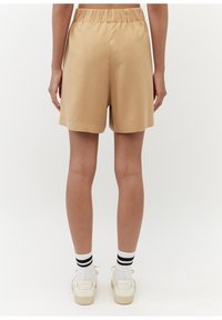 Beige skräddarsydda shorts med ett elastiskt midjeband, som når till mitten av låret, slät textur, rak benform, matchat med vita strumpor och skor.