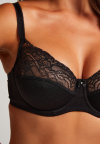 Zwarte beha met kantafwerking en stippenpatroon, gekenmerkt door een strikaccent in het midden, verstelbare bandjes en een gladde onderband.