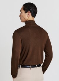 Brauner Rollkragenpullover mit taillierter Passform und strukturiertem Strick, kombiniert mit beigefarbenen Hosen und einem schwarzen Gürtel, von hinten betrachtet.