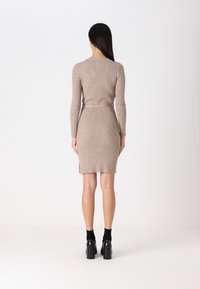 Robe tricotée beige avec des manches longues, un tricot texturé, une silhouette ajustée, des fentes latérales et une ceinture assortie. Assortie à des chaussures à talons carrés noires.